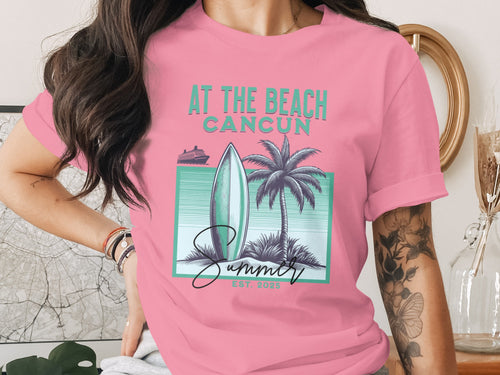Pink t-shirt with "AT THE BEACH CANCUN SUMMER EST. 2025" and beach graphic.